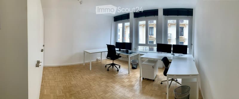 modern workspace with 3 white desks, black swivel chairs, 2 trash bins, and large windows