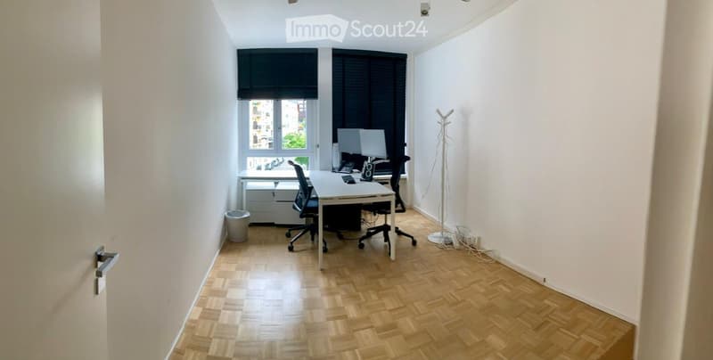 office room with wooden floor, white walls, desk, monitors, office chair, storage boxes, trash bin
