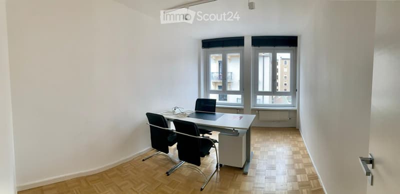 Office with white walls, wooden floors, desk, two chairs, open door, windows with view