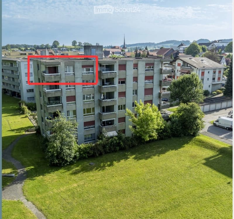 Apartment building, red and grey brick facade, windows, multiple balconies, central pathway, green lawn area