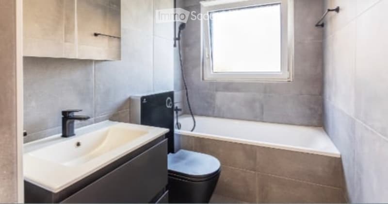 White bathroom with grey tile, bathtub, toilet, sink