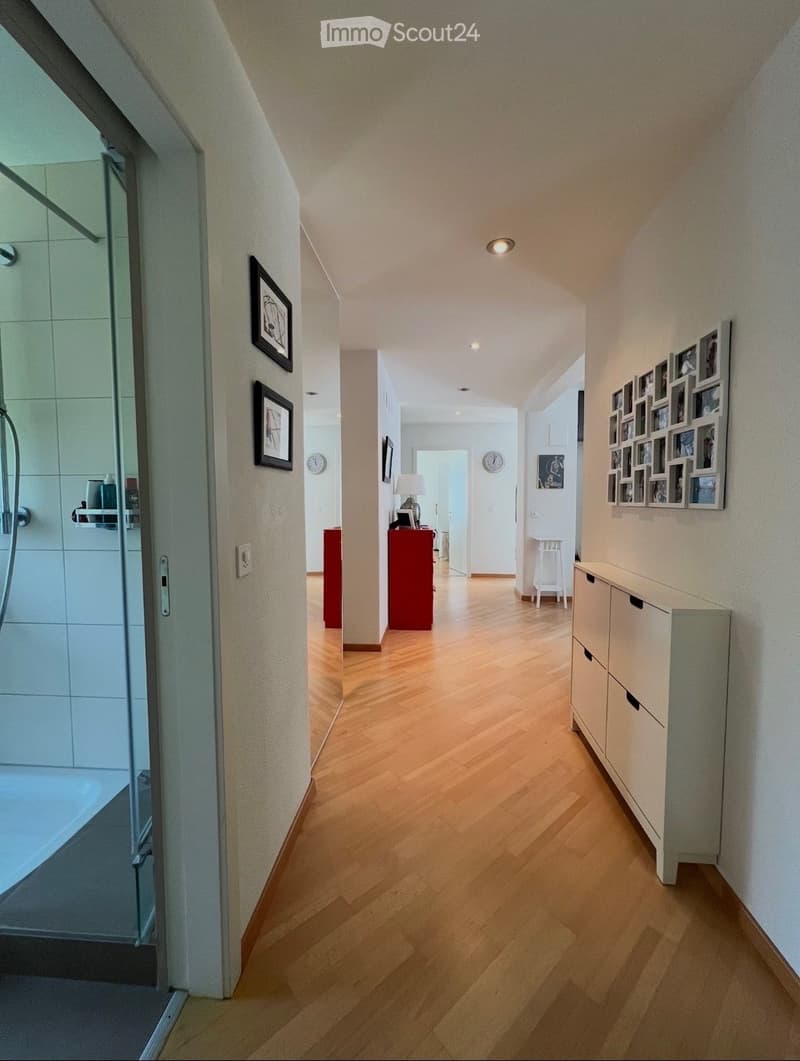 Wooden floor, white walls, gallery of pictures, open door leading to bathroom, hallway with storage cabinet