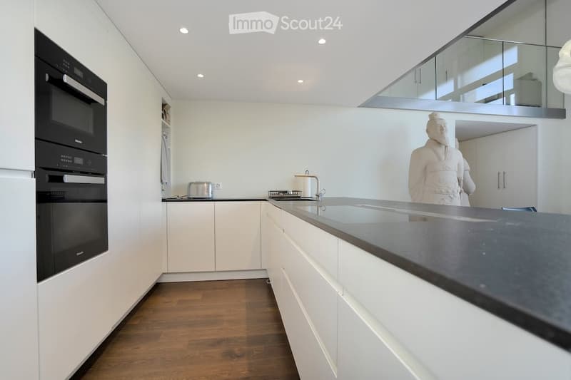 modern kitchen, white cabinetry, black countertops, integrated oven and microwave, granite backsplash, white subway tile, glass window, silver faucet, white statue, wooden floors