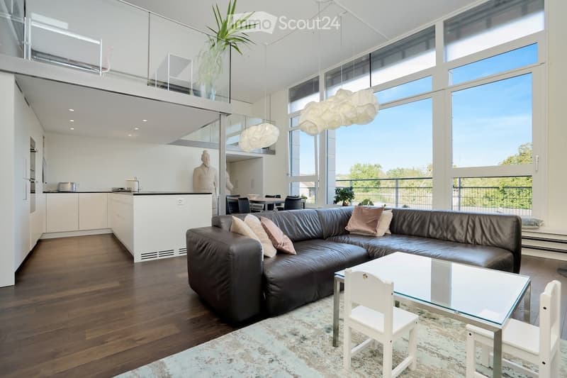 Open plan living space with living room and kitchen, large windows, balcony, and ceiling lamps