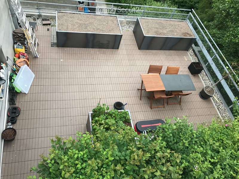 Balcony with wooden decking, wooden chairs and table, raised flower pots, green plants, ladder, fenced boundary, fenced view to the surrounding area