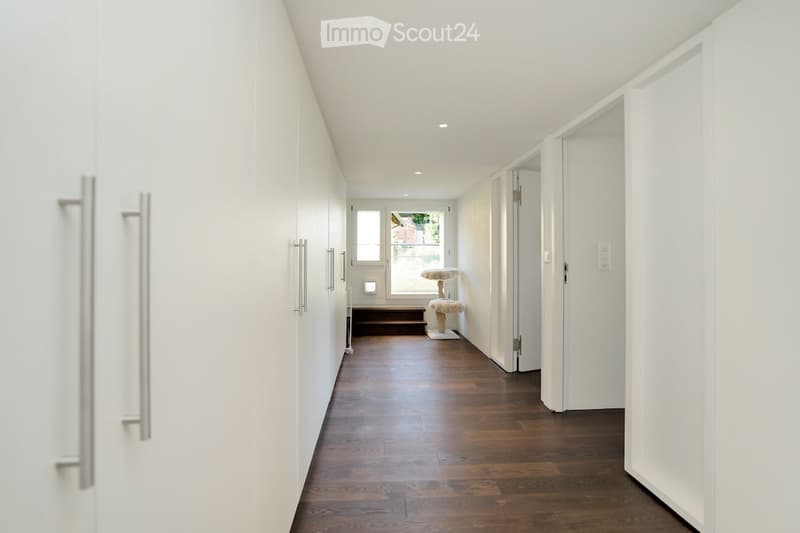 White cabinets, wooden floor, bright lighting, open door at the end.