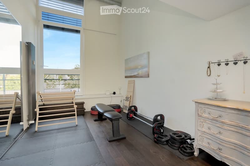 A workout room with a bench, dumbbells, a mirror, and exercise mats. The room features a window with blinds and an artwork on the wall. A cabinet with drawers is placed in the corner.