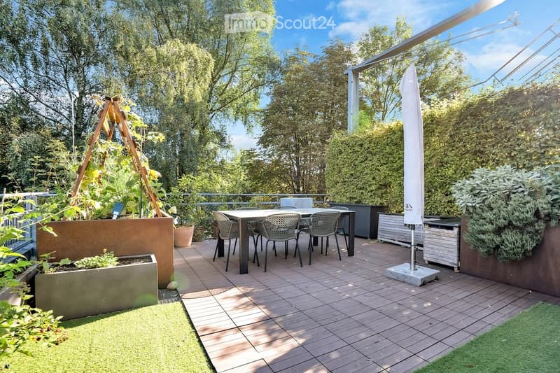 wooden deck with table and chairs, potted plants, raised beds, artificial turf, metal fence, greenery