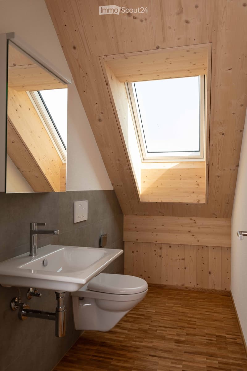 A bathroom with wooden walls, hardwood floor, white sink, mirror, white toilet, and a window.