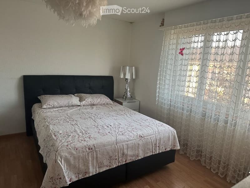 Double bed with a floral bedding, lamp, pillow, nightstand with a lamp, curtains