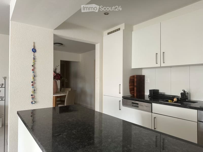 Modern kitchen with white cabinets, black granite countertop, stainless steel appliances, and a small dining area visible in the background.