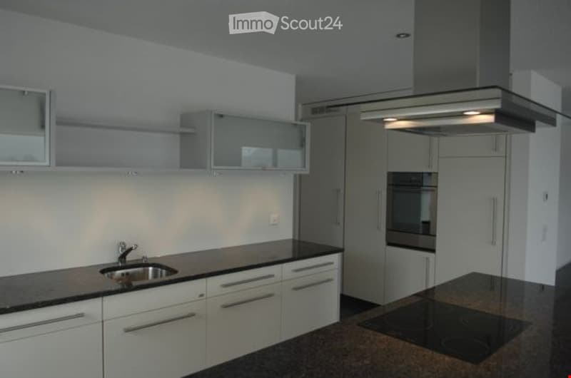 Modern kitchen with granite countertops, stainless steel sink, white cabinets, oven, and integrated range hood.