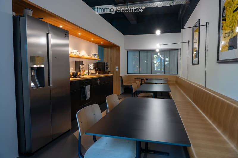 Modern kitchen and dining area with stainless steel appliances, wooden shelves, and seating area with tables and chairs.