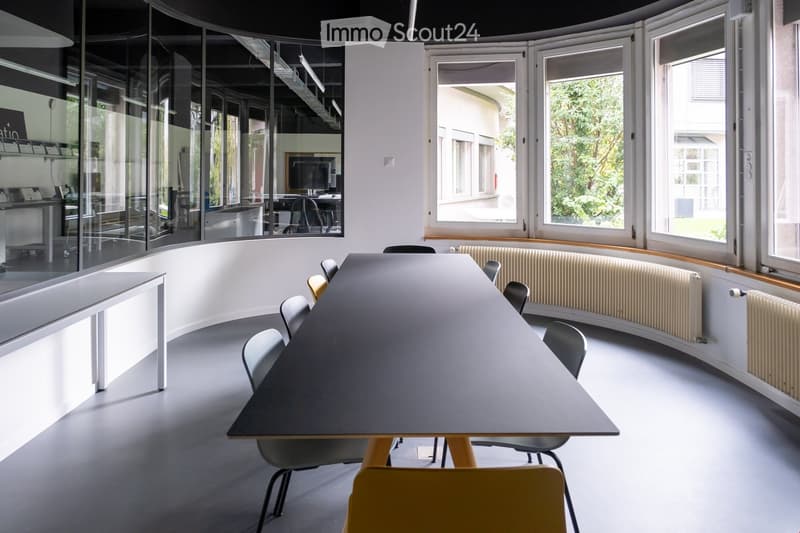 Modern meeting room with large windows, long table and chairs, white walls and gray flooring