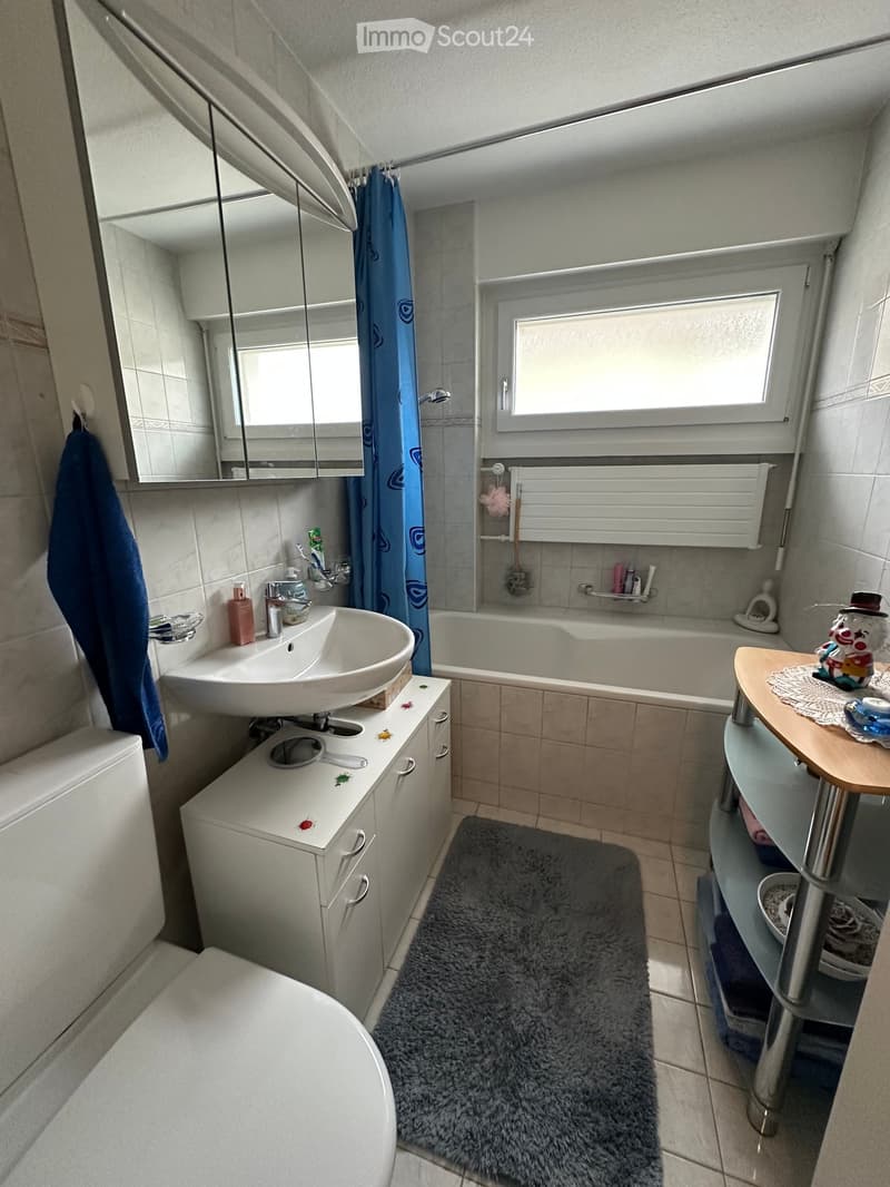 modern bathroom, white tiles, bathtub, white vanity, sink, white cabinets, white toilet, shower curtain, towel racks, shower head, towels, and storage shelves