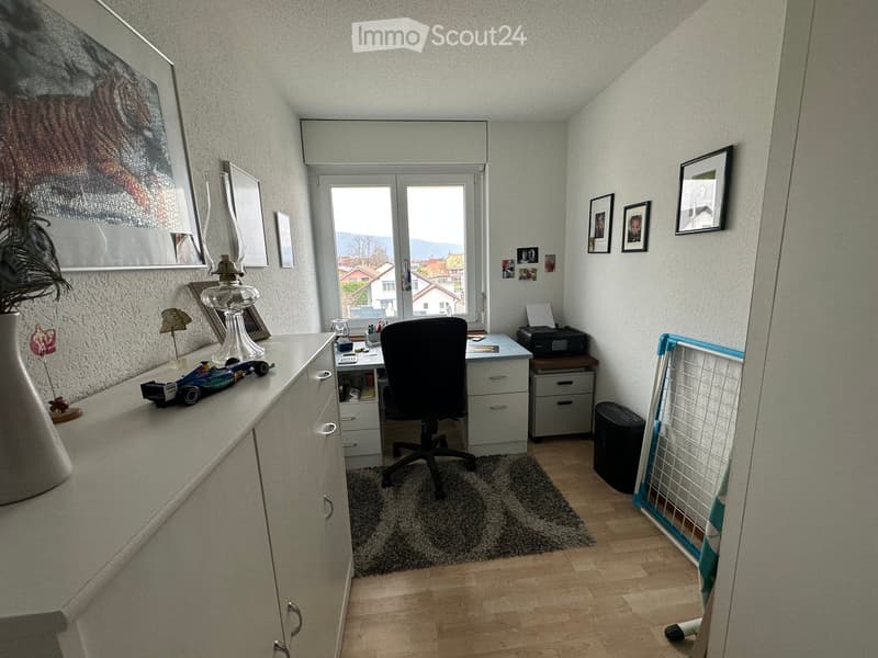 desk with chair, black printer, black trash bin, white cabinets, carpet, toy cars, framed photos, window with view
