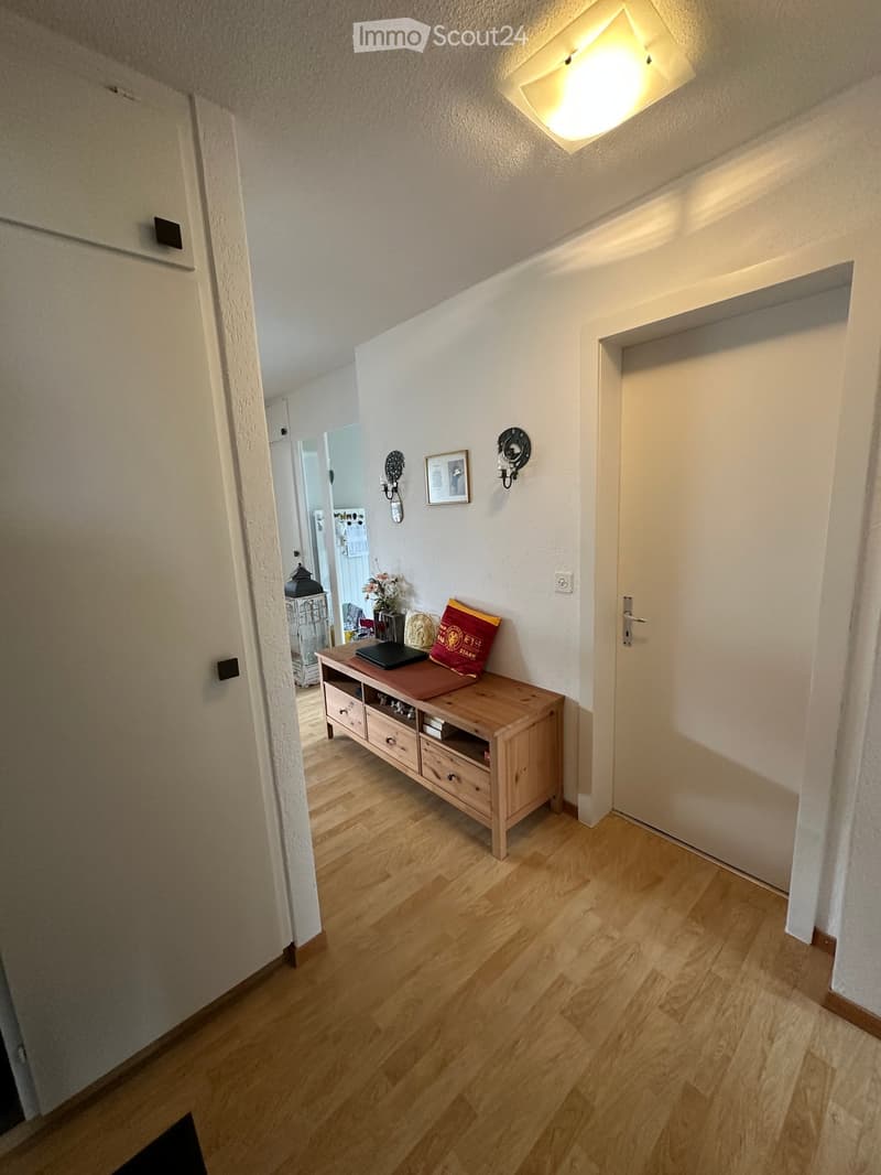 Entrance hall with wooden floor, wooden console table, wall decorations, open door leading to another room
