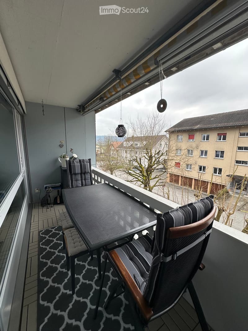 Balcony with dining table, 2 chairs, decorative items, black and white rug, building view, tree