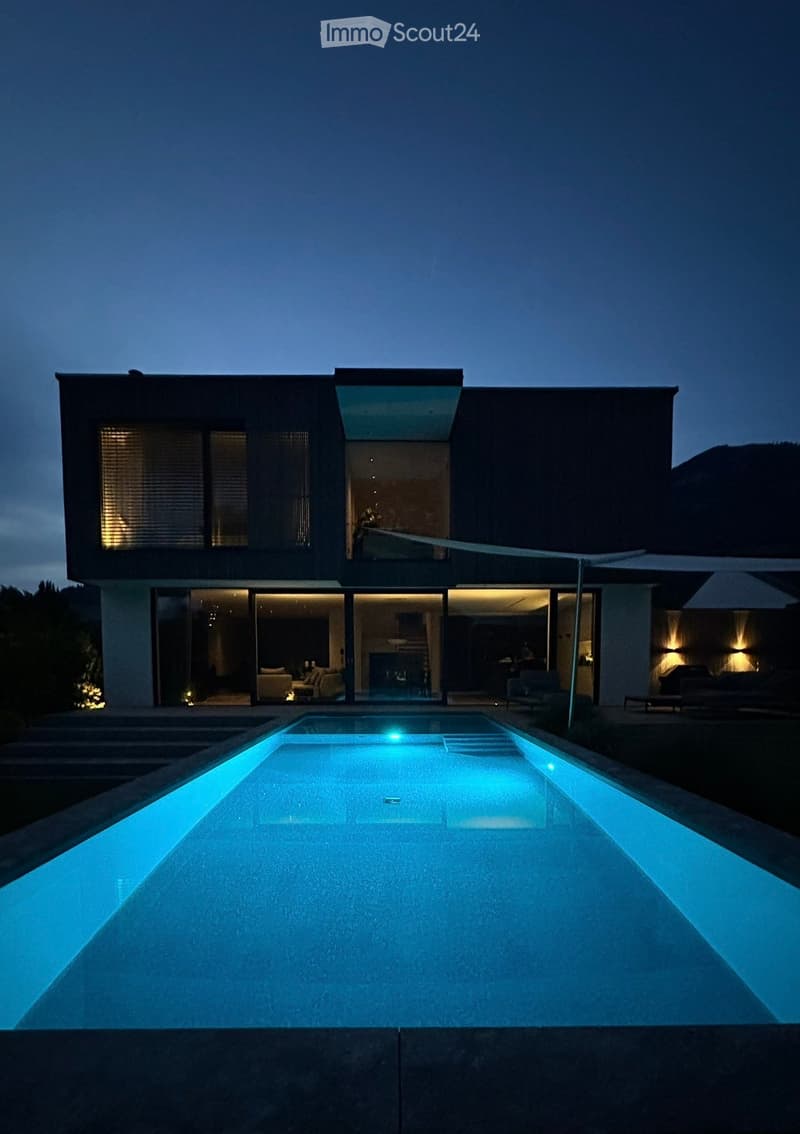 modern house with glass walls, pool, outdoor patio area, lit at night
