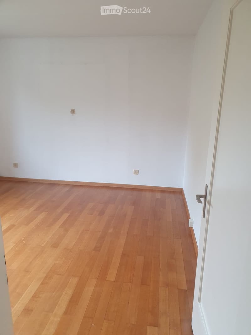 empty room with hardwood floor, white walls, power outlets, closed door