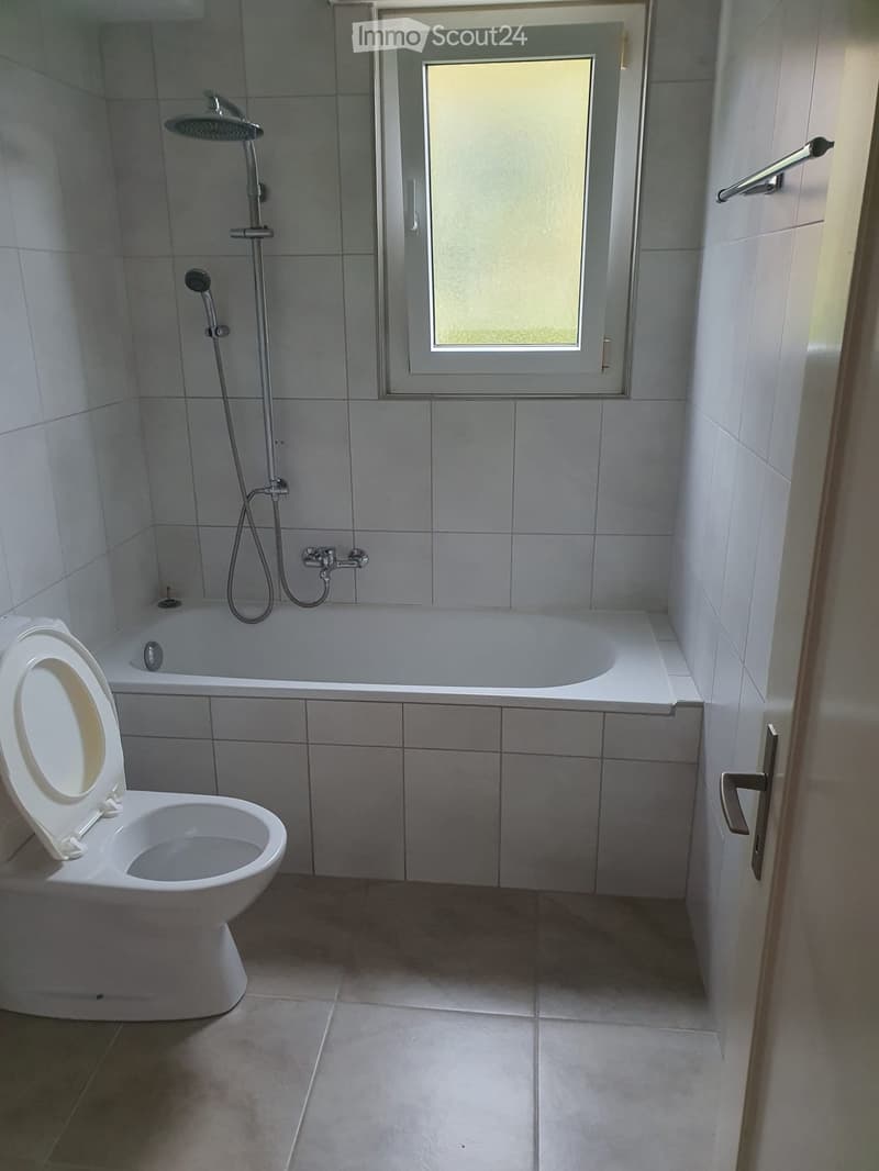 white tiled walls, floor and tub, white toilet, glass door, window, shower