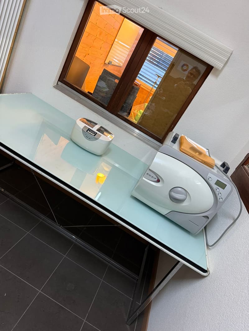 A kitchen counter with a glass top, a toaster, a rice cooker, and a white wall behind it.