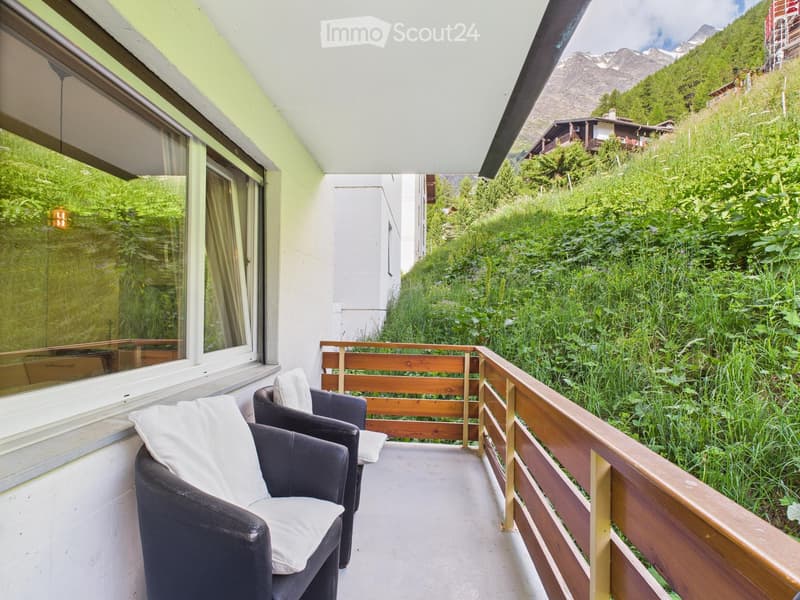balcony with wooden railings, leather chairs, cushions, mountain view, wooden floor