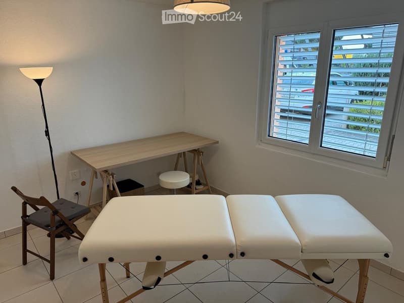 A room with massage table, wooden chair, small table, stool, wall lamp, desk, power outlets.