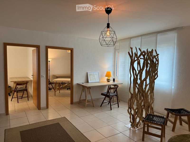 large room, white tiles, white walls, wooden desk, wooden chairs, lamps, rug, large art installation
