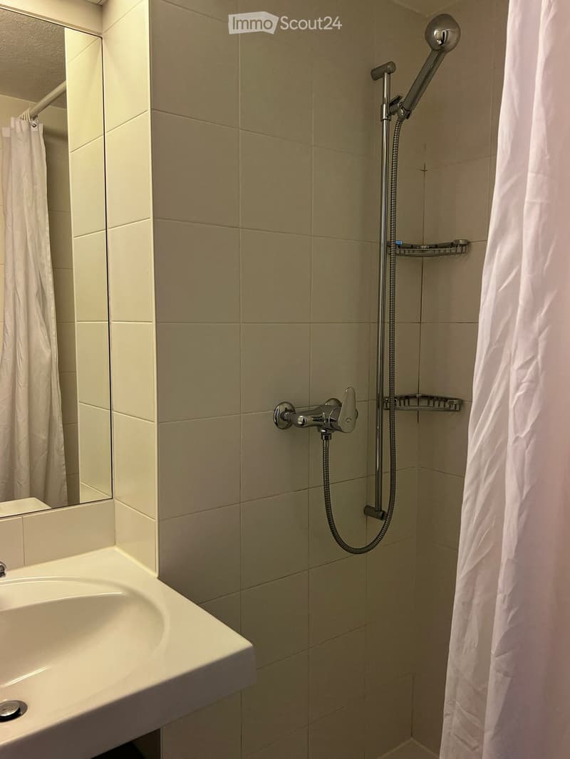 Tiled shower with shower head, white sink with vanity, silver faucet, mirror with shower curtain, white shower curtain