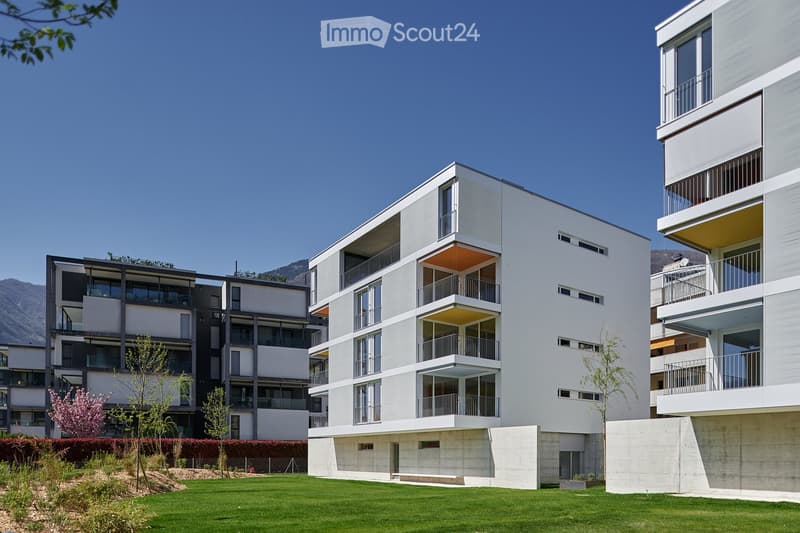 modern multistory building with multiple balconies and windows, surrounded by a grassy lawn and trees