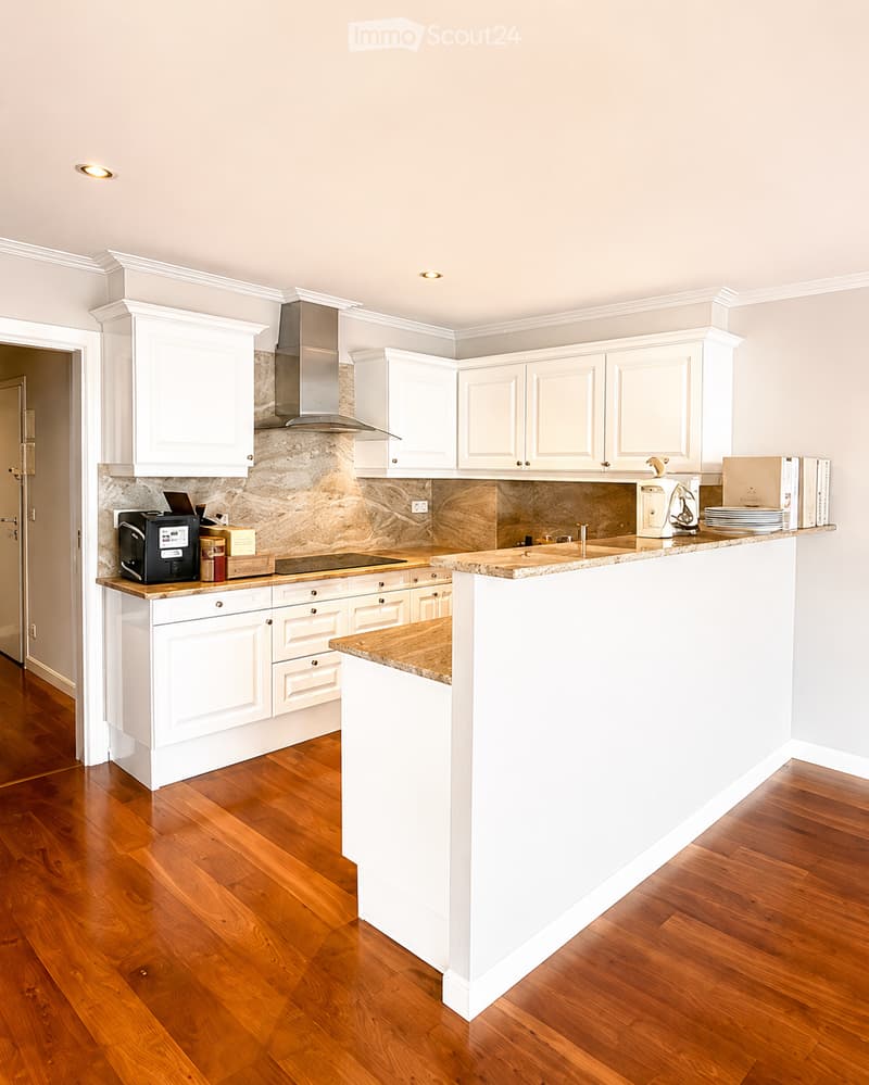 Kitchen. Modern kitchen with white cabinets, wooden flooring, and a central island. Features include a coffee maker, oven, fridge, and various kitchen items on the counter.