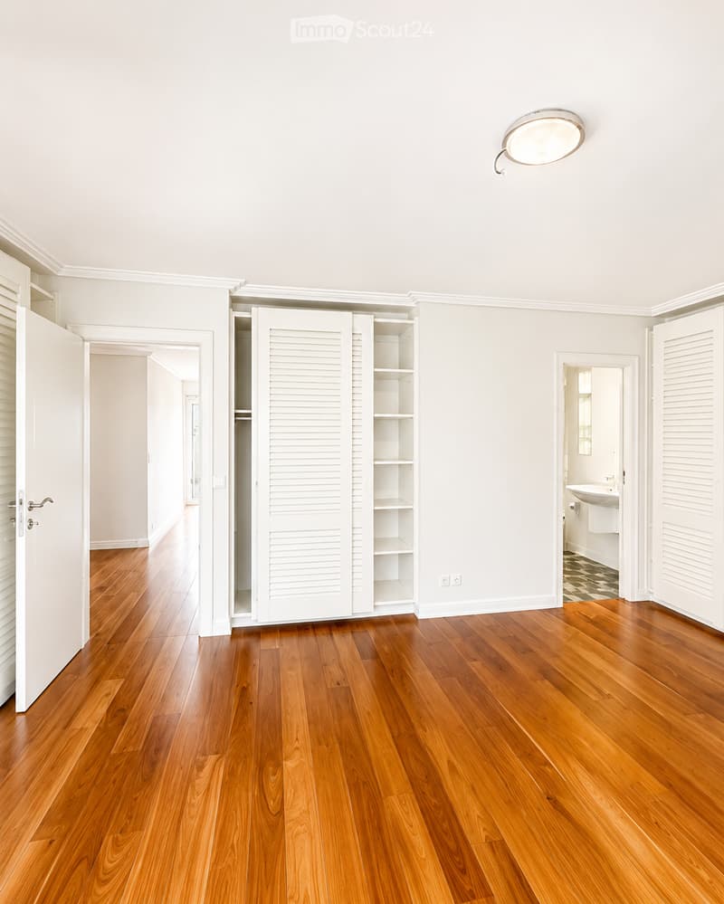 Unfurnished Room. Empty hallway with polished wooden floors, white walls, and built-in closet with open shelving. A bathroom is visible at the end of the hallway.