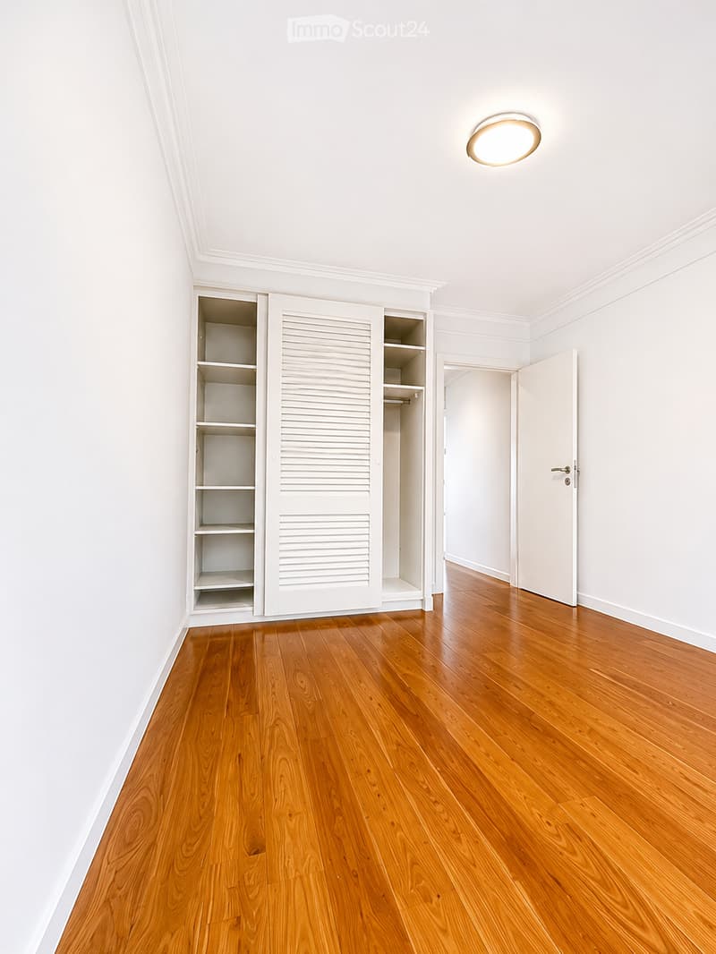 Unfurnished Room. Empty room with wooden flooring, white walls, built-in closet with open shelving, and a round ceiling light fixture.