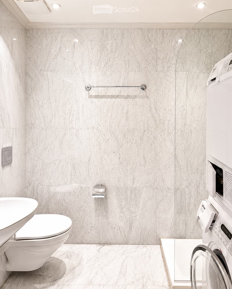 Bathroom. Modern bathroom with marble tiles, a toilet, a washing machine, a towel rack, and a toilet paper holder.