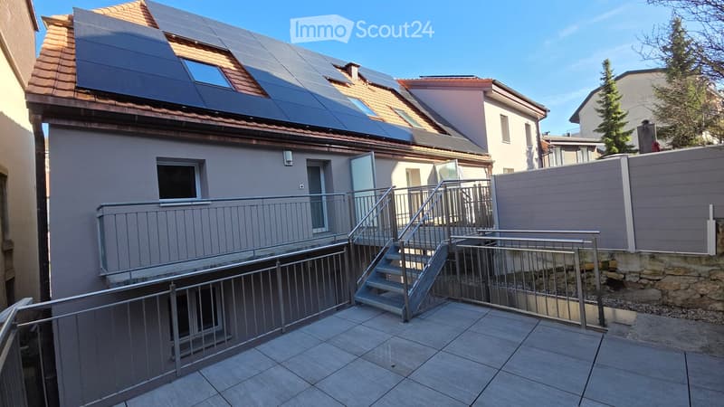 3 story building with red tiled roof, solar panels, staircase leading to a balcony with railings, small stone wall on the side