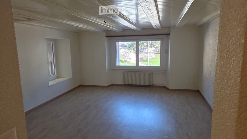 Empty room with wooden floors, white walls, large window, radiator, window sill