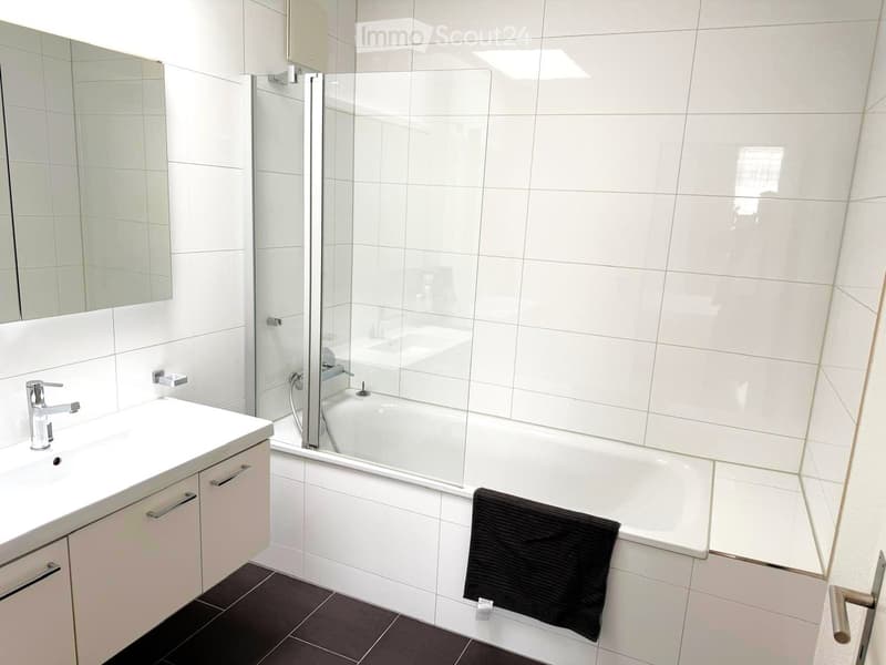 white bathtub, glass shower door, white vanity with sink, white tiles, towel rack