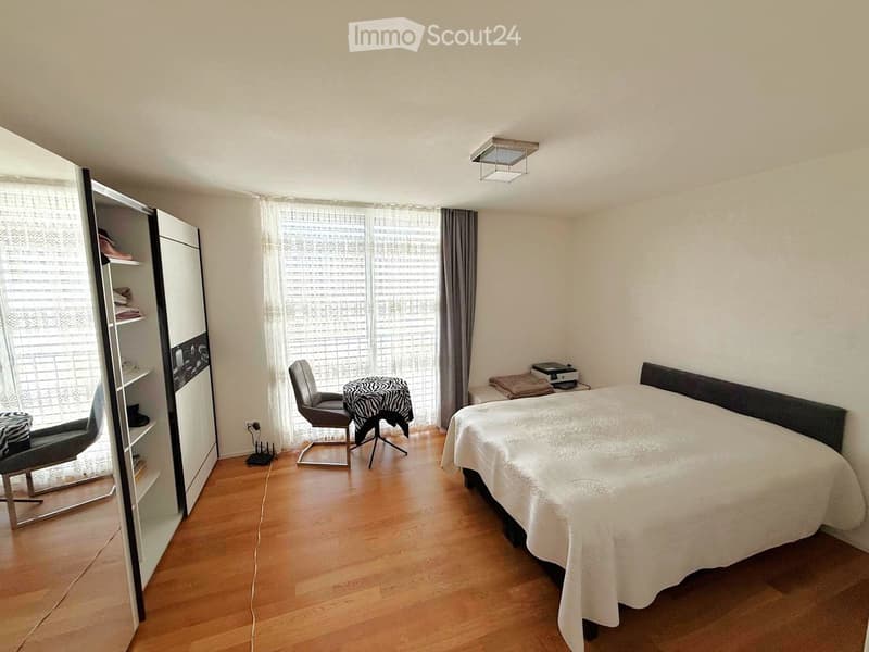 Bedroom with double bed, grey chair, round table, and a built-in wardrobe with shelves
