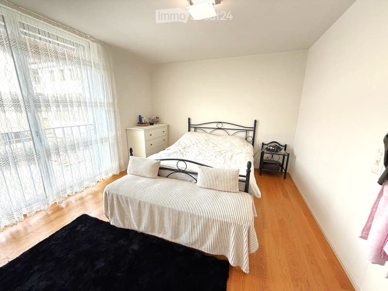 bedroom with a bed, pillow, mattress, carpet, cabinet, bedside table, lamp, sofa, window, and curtain