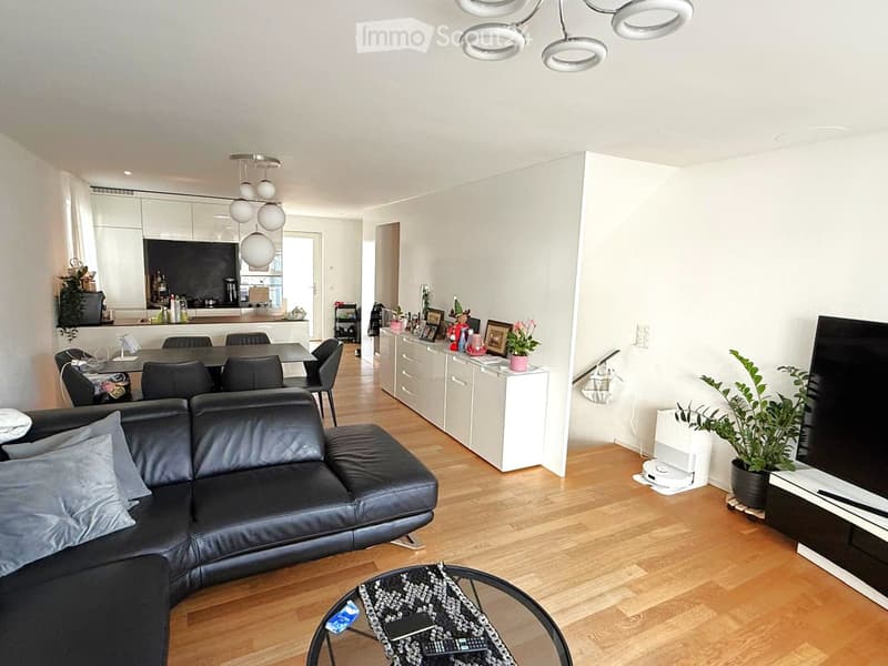 open floor plan, modern design, black leather couch, wooden flooring, dining table and chairs, white kitchen cabinets, chandeliers, plants, smart TV