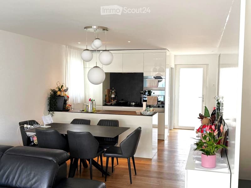 modern interior with a dining area and a kitchen island, black leather chairs, wooden flooring, modern pendant lights, white cabinets, a counter with plants and a coffee machine