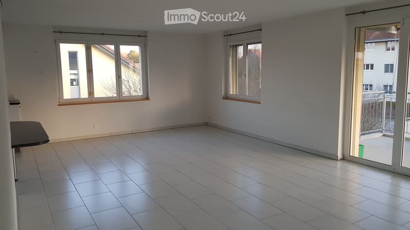 Empty room with white tiles, two windows, glass doors leading to a balcony with railings