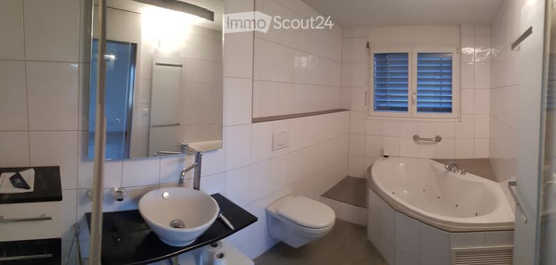 Modern bathroom with a bathtub, separate toilet, sink, and shower. Fully tiled with white tiles and a glass shower enclosure.