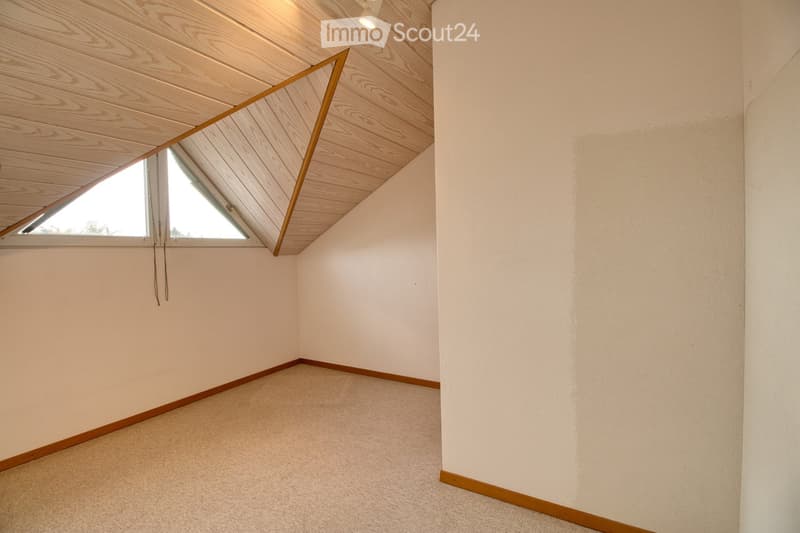empty attic room with ceiling light, carpet, triangular window