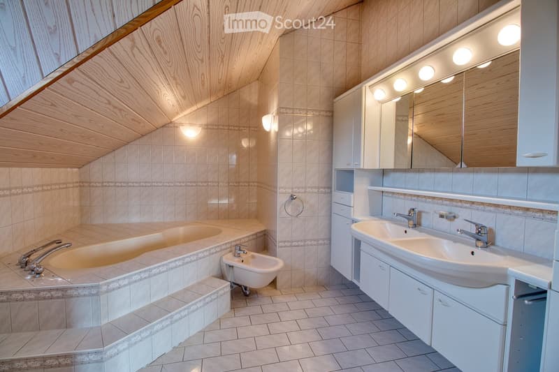 white tile walls, large bathtub, bidet, vanity with double sink, wooden ceiling, large mirror, built-in cabinets