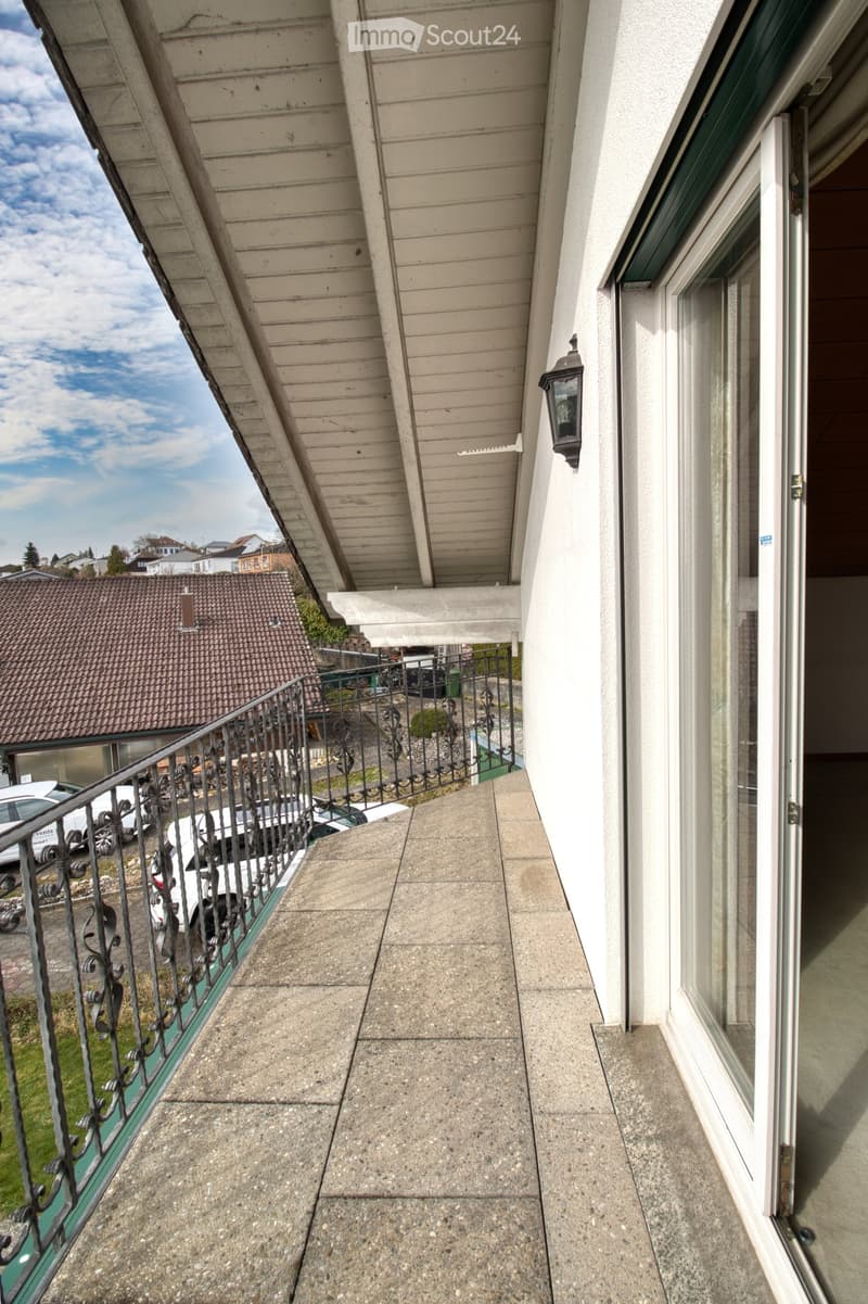 A balcony with green railings, paved floor, and a wall with a sliding door.