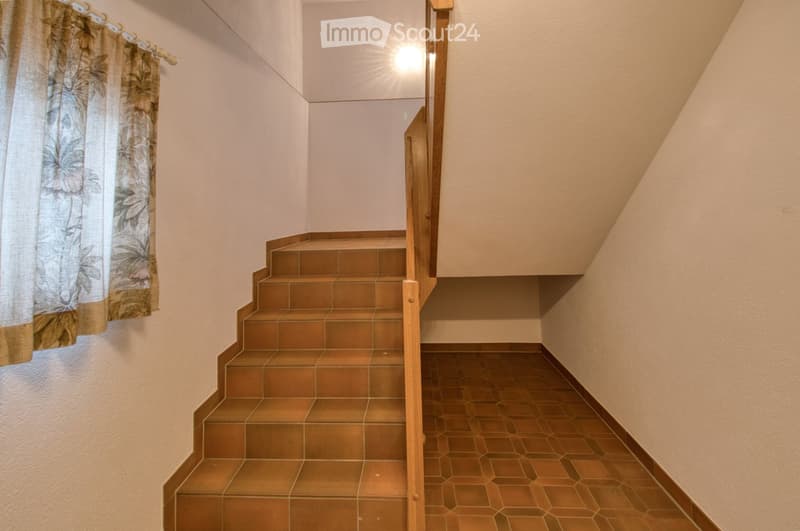 Image of staircase in a building with brown tile steps and wooden handrail