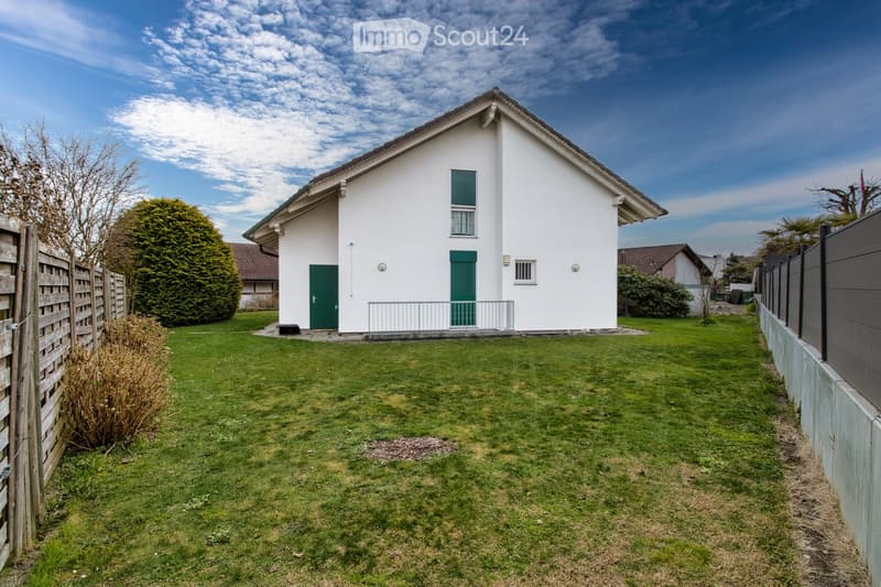 Single-family house, white exterior, green doors, metal railing, fenced yard, green lawn, shrubs, trees