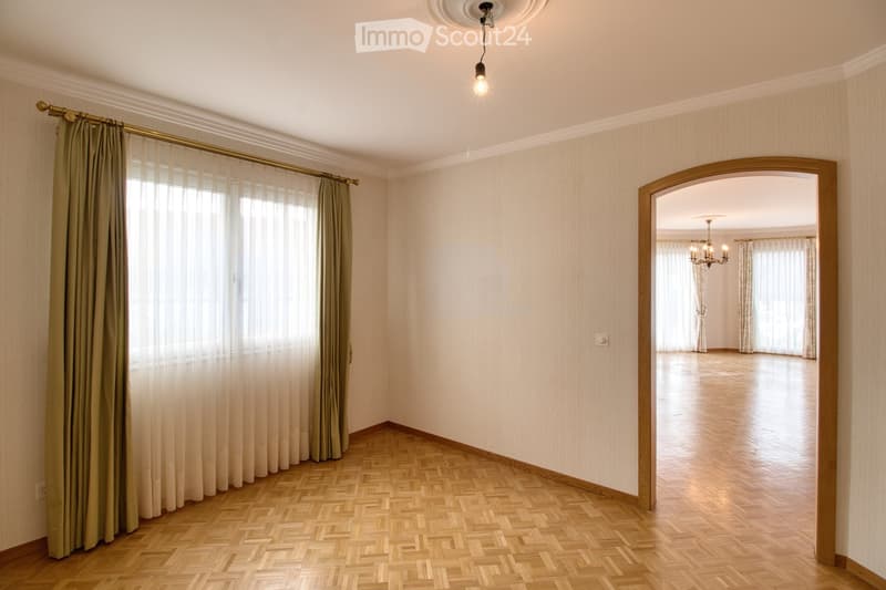 Spacious room with parquet floor, white walls, curtains, chandelier, doorway to another room